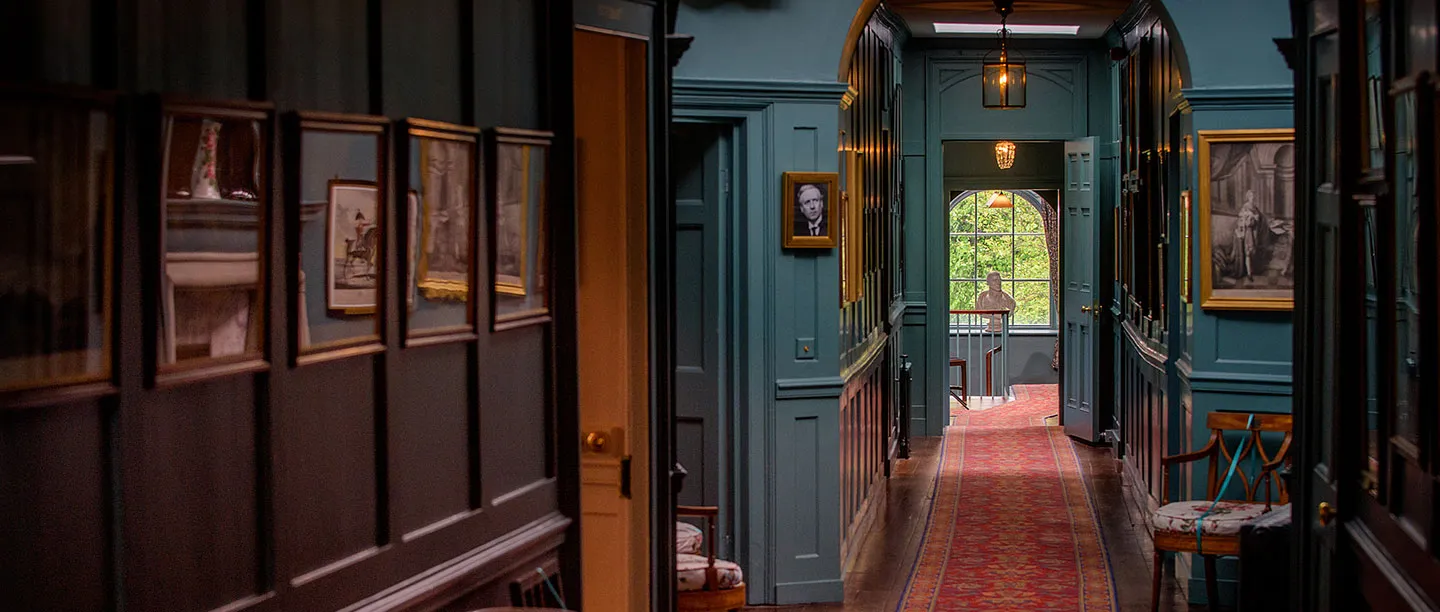 A panelled corridor hung with prints, leading to a bust at the landing window