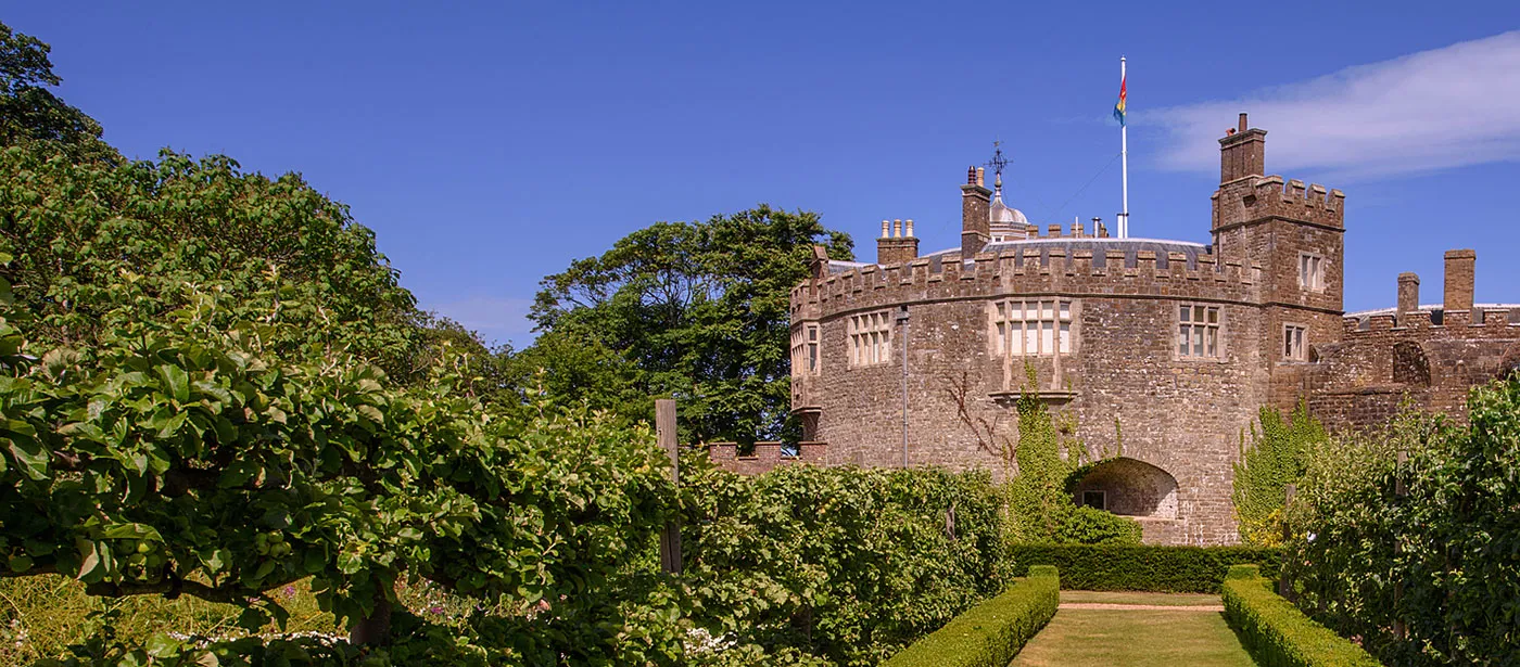 The castle's battlemented tower and flagpole at the end of a hedged garden walk