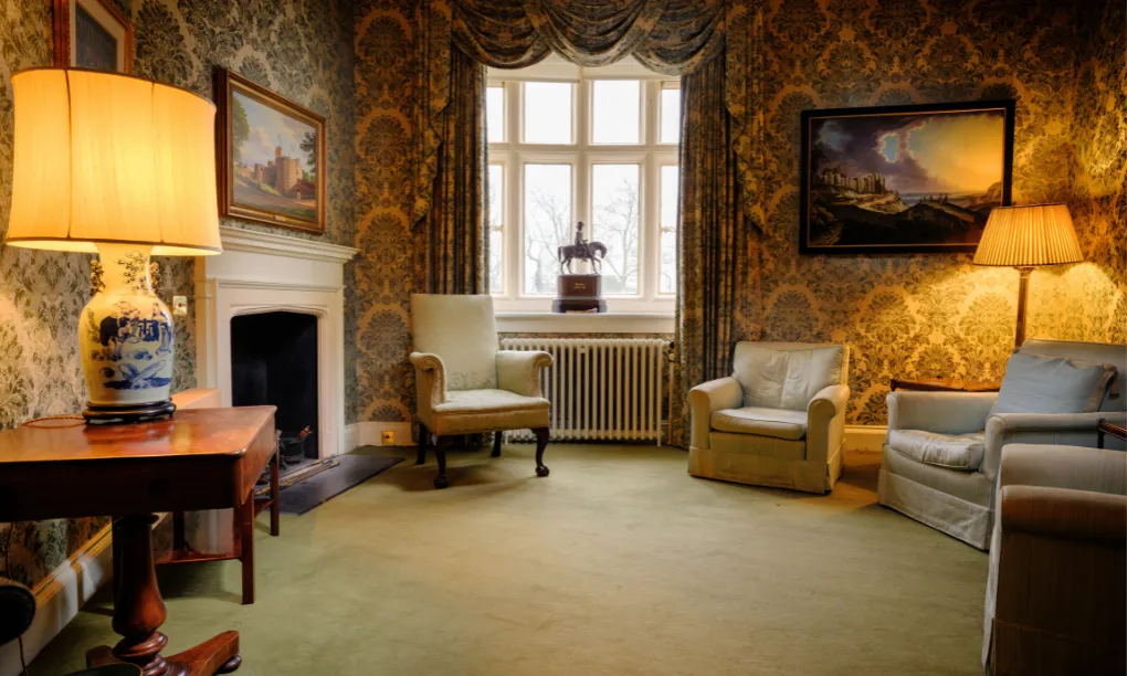 The Lord Warden's sitting room, with damask walls, lamps and a painting of a castle