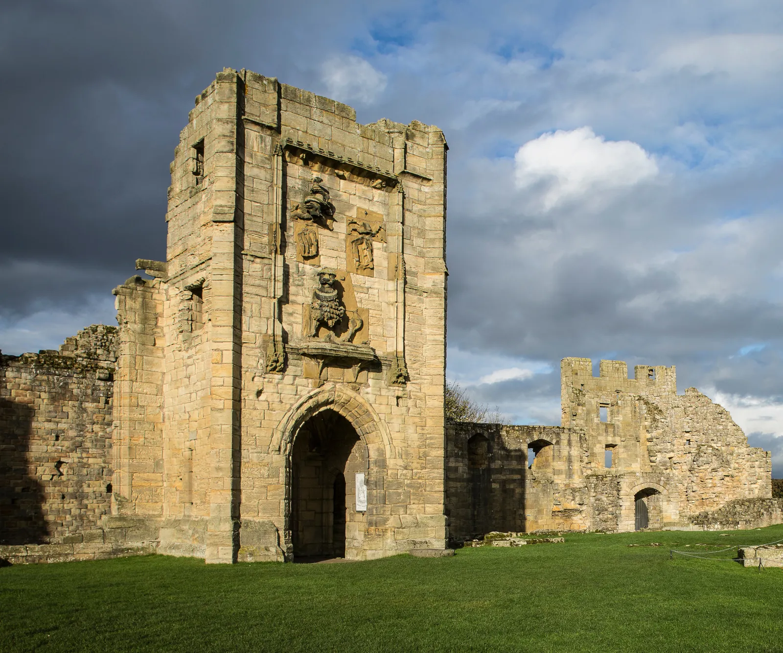 The gatehouse to the great hall, carved with the Percy lion, under a dark storm sky