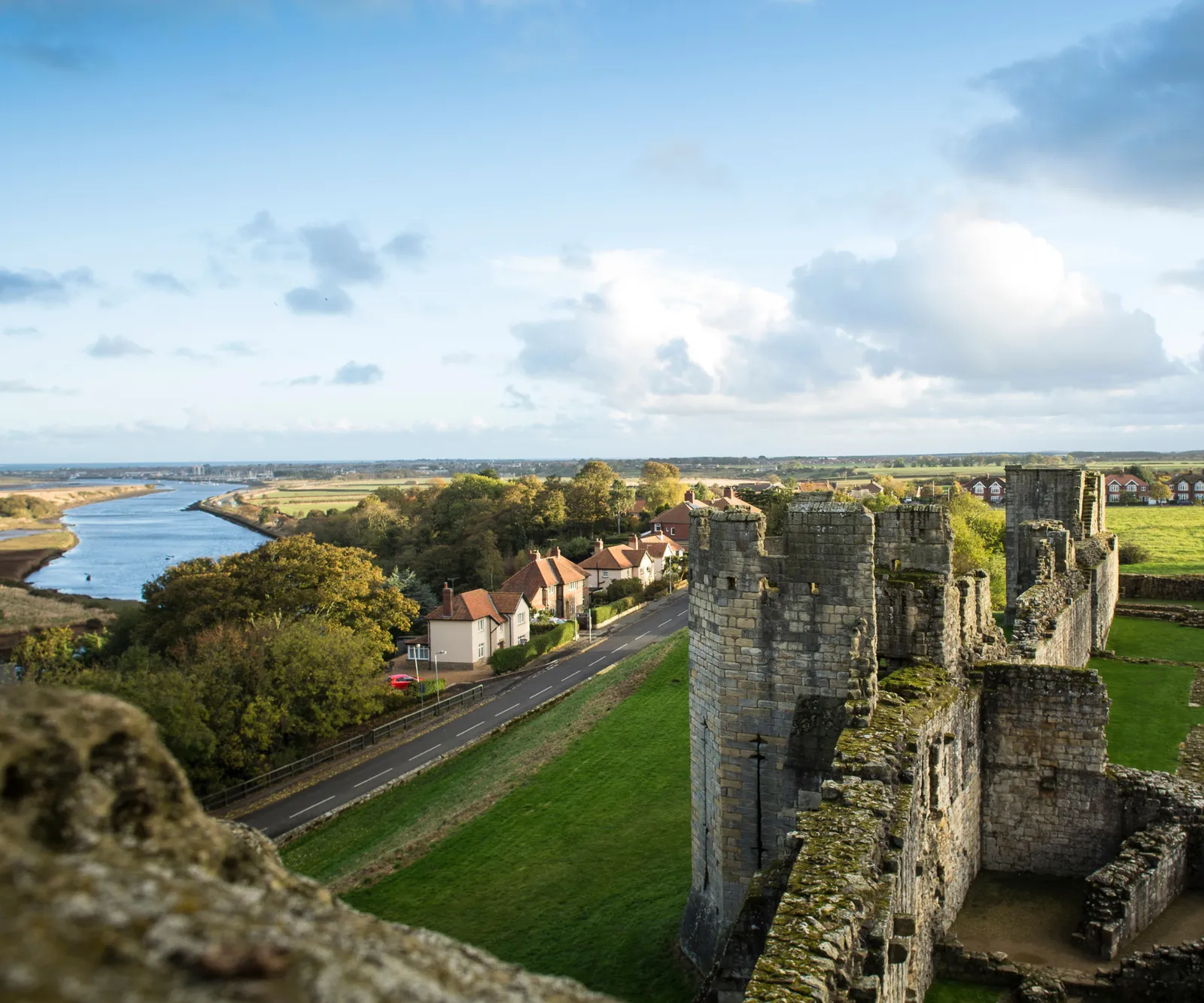 Looking down from the great tower over the curtain wall towers and the River Coquet winding to the sea