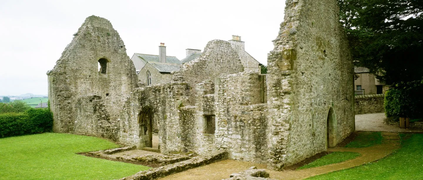 The ruined stone walls and gables of Warton Old Rectory on a lawn, with the church and village houses behind