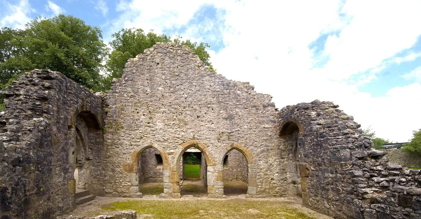 The tall rubble gable wall of Warton Old Rectory's great hall with three pointed service doorways, under a summer sky