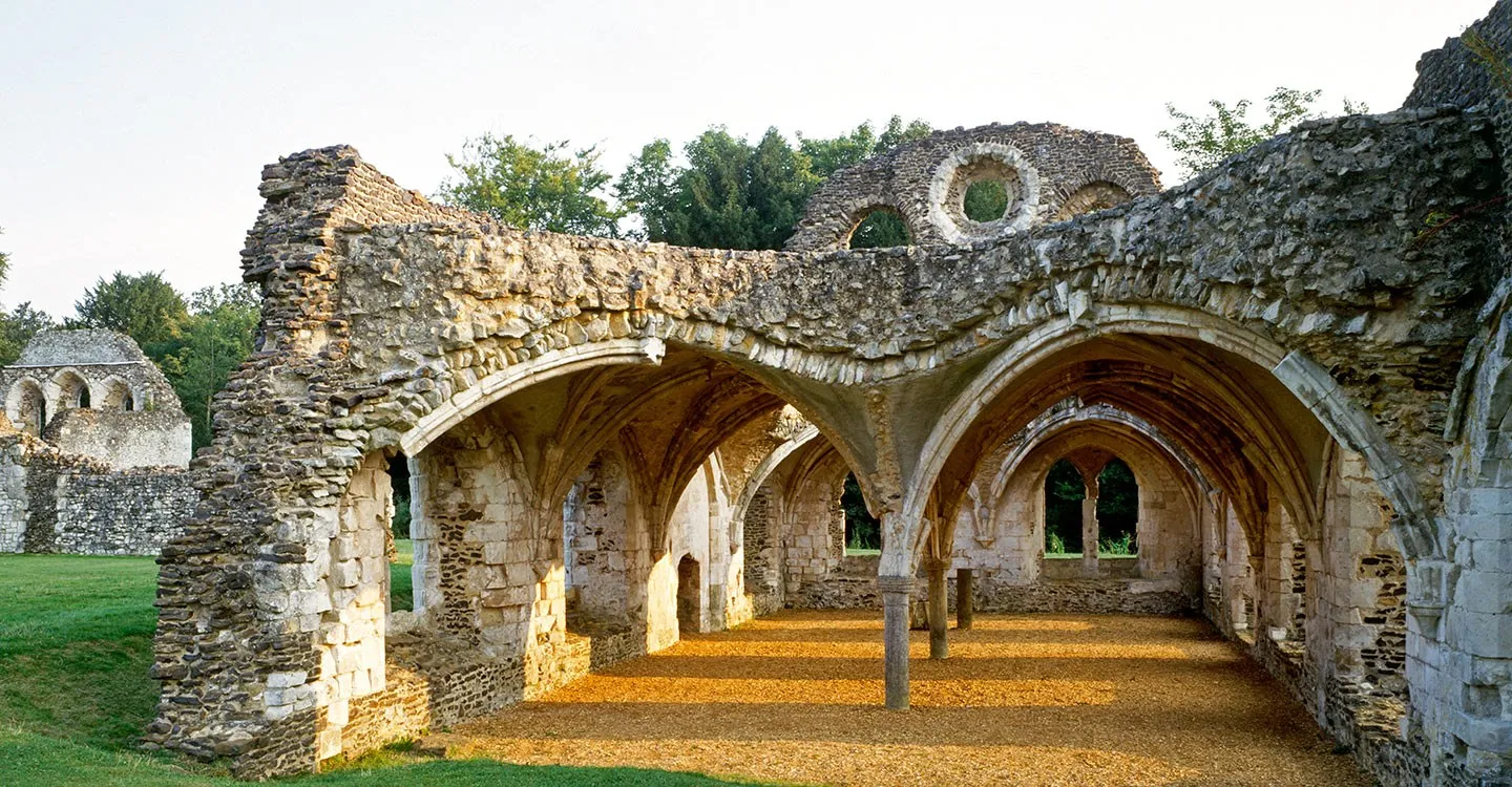 The vaulted undercroft at Waverley Abbey, with a golden gravel floor and arches lit by evening sun