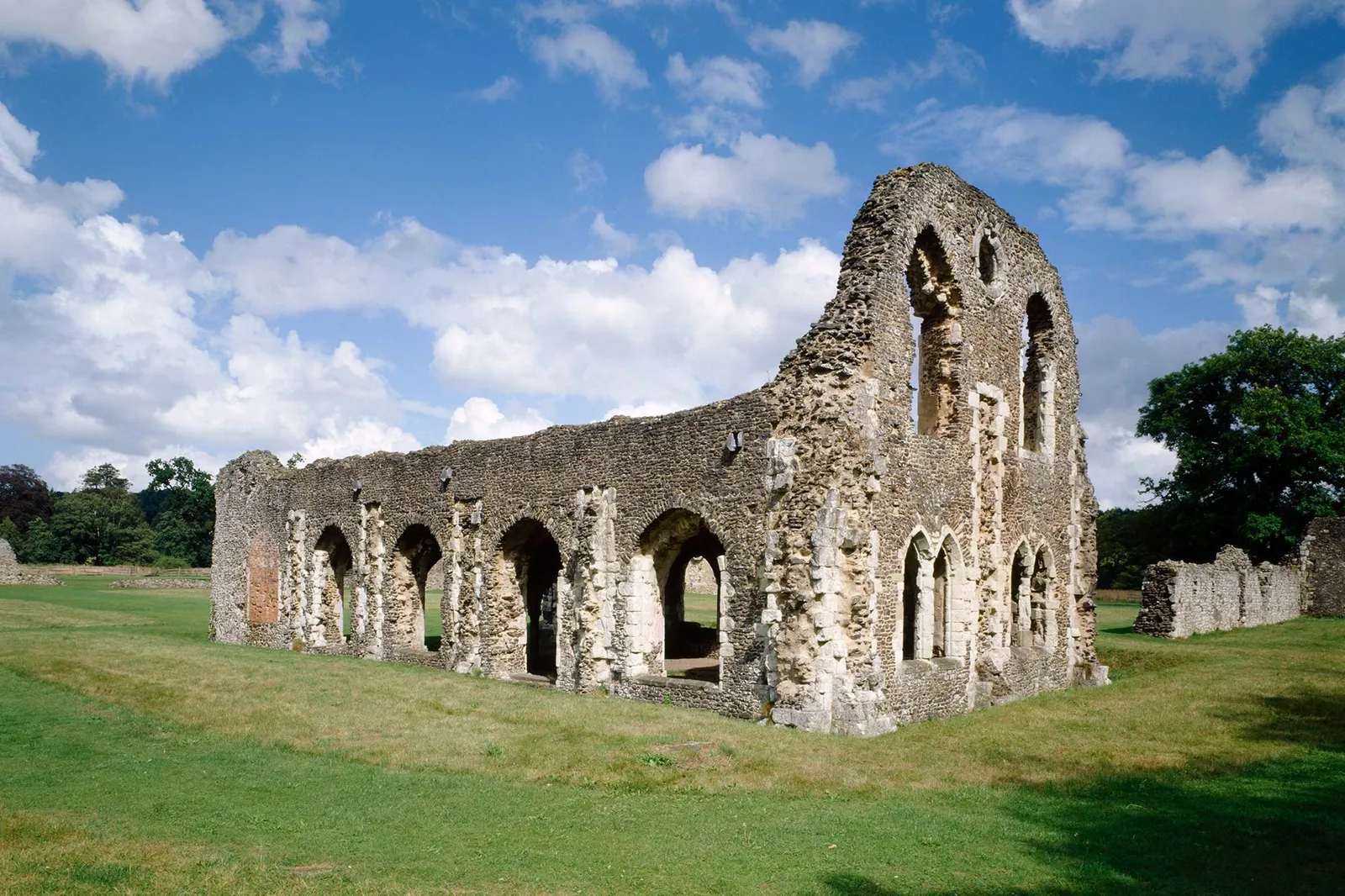 The arcaded lay brothers' range of Waverley Abbey across a green lawn, with a ruined gable against the sky