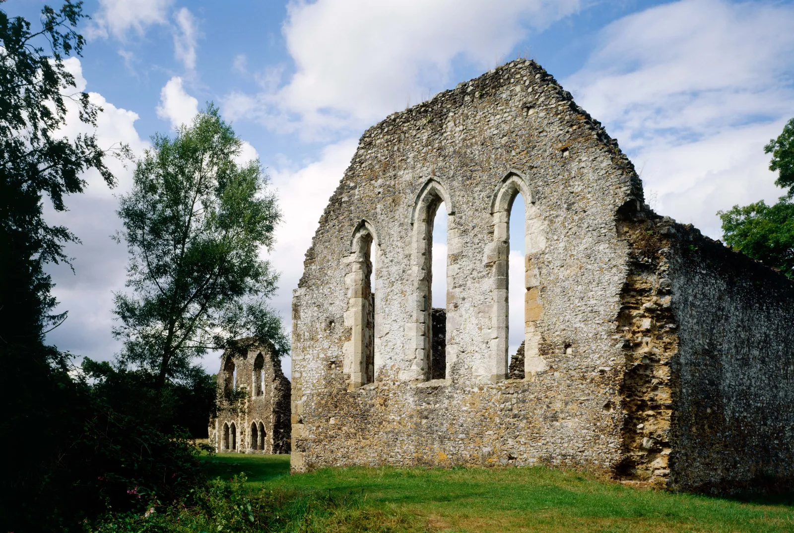 Lancet windows in the flint and stone walls of Waverley Abbey with trees and a cloudy sky