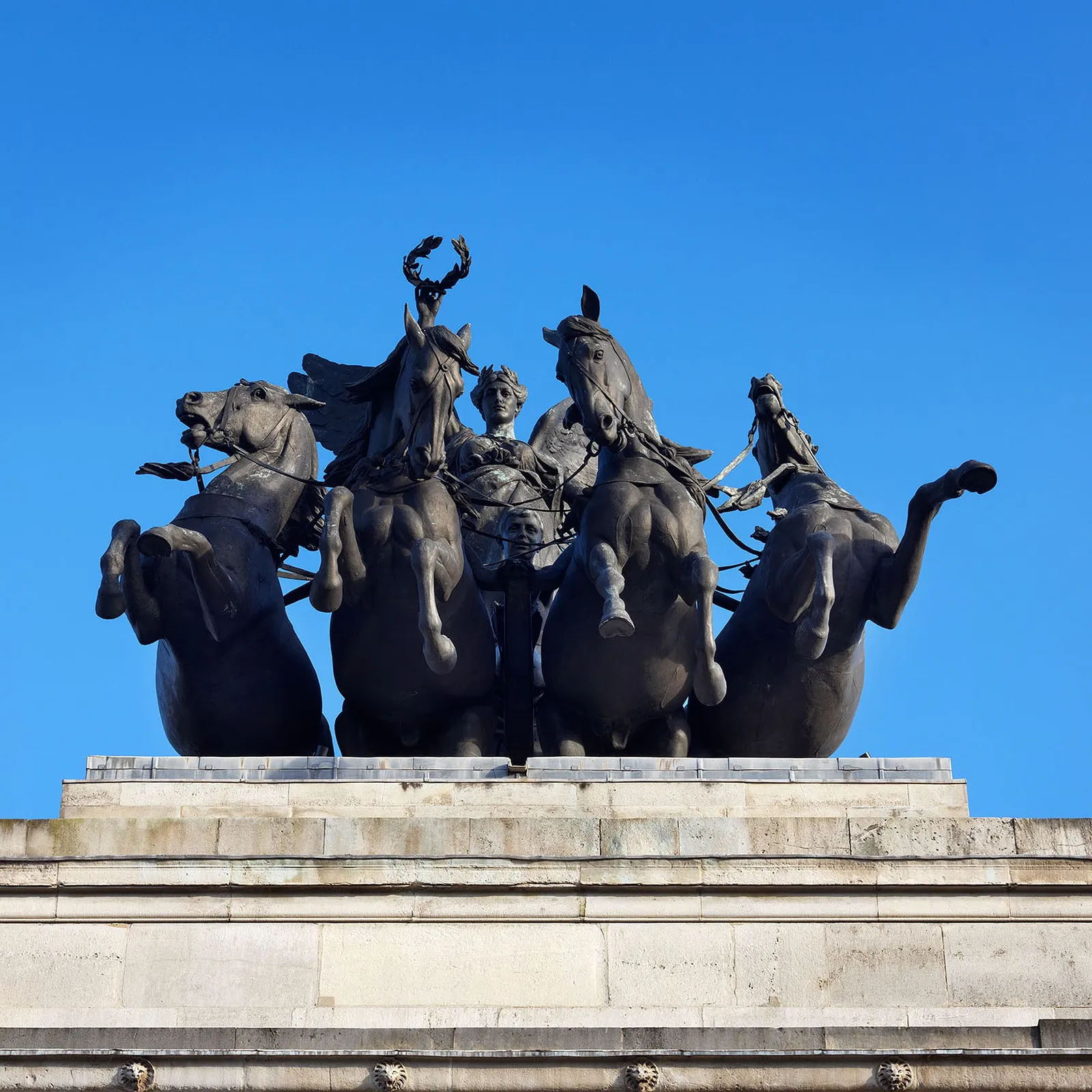 The bronze quadriga of Peace and four rearing horses on top of the arch against a deep blue sky