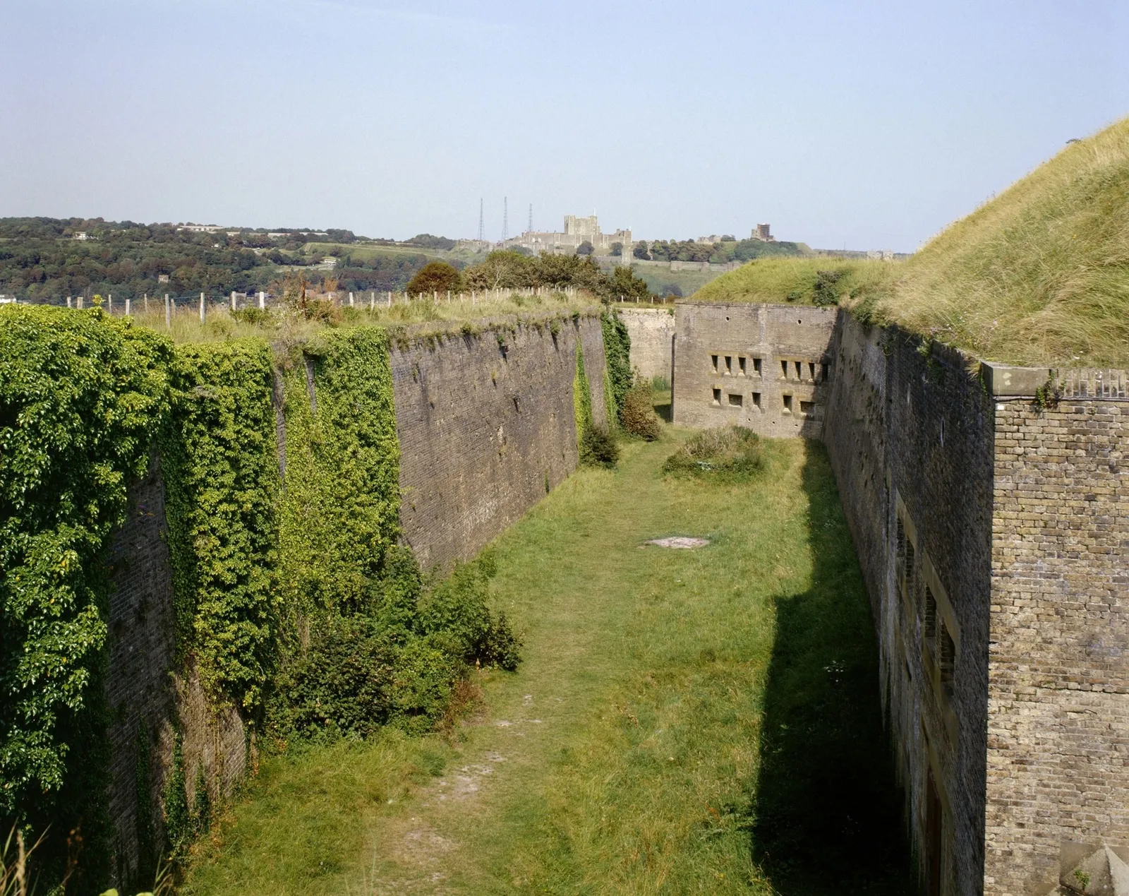 The deep brick-walled ditch of Western Heights, overgrown with ivy, with Dover Castle on the hill beyond