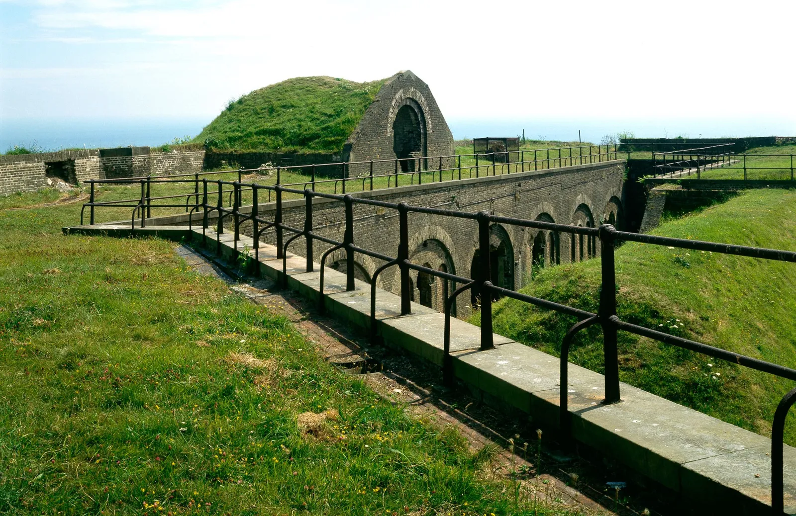 Iron railings above the brick casemate arches of the Drop Redoubt at Western Heights, with grassy ramparts and the sea beyond