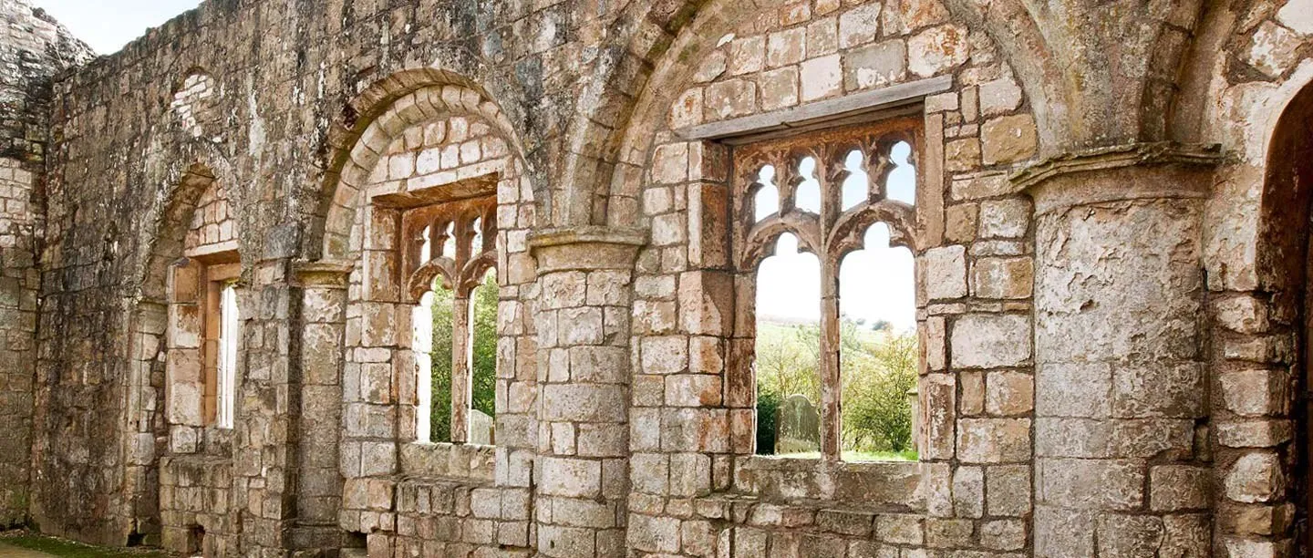 Round-arched windows with Gothic tracery in the ruined nave wall of Wharram Percy church, looking out to the churchyard