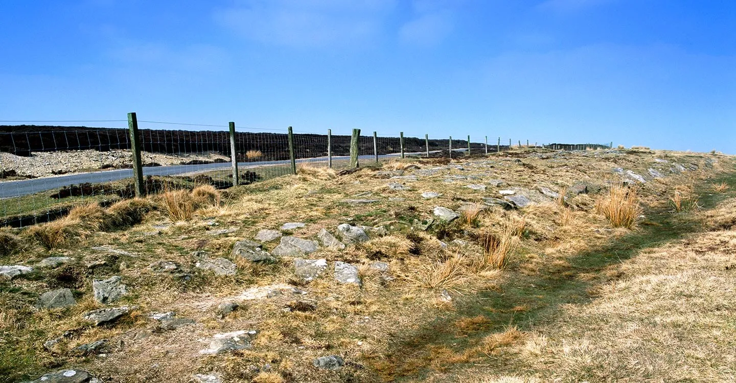 The exposed stones of Wheeldale Roman Road running beside a wire fence and a moorland lane under a deep blue sky