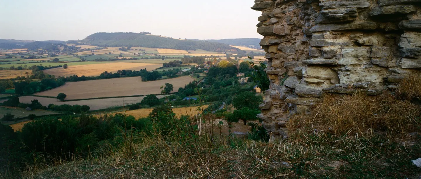 The ruined walls of Wigmore Castle looking down over Wigmore village, golden fields and wooded hills