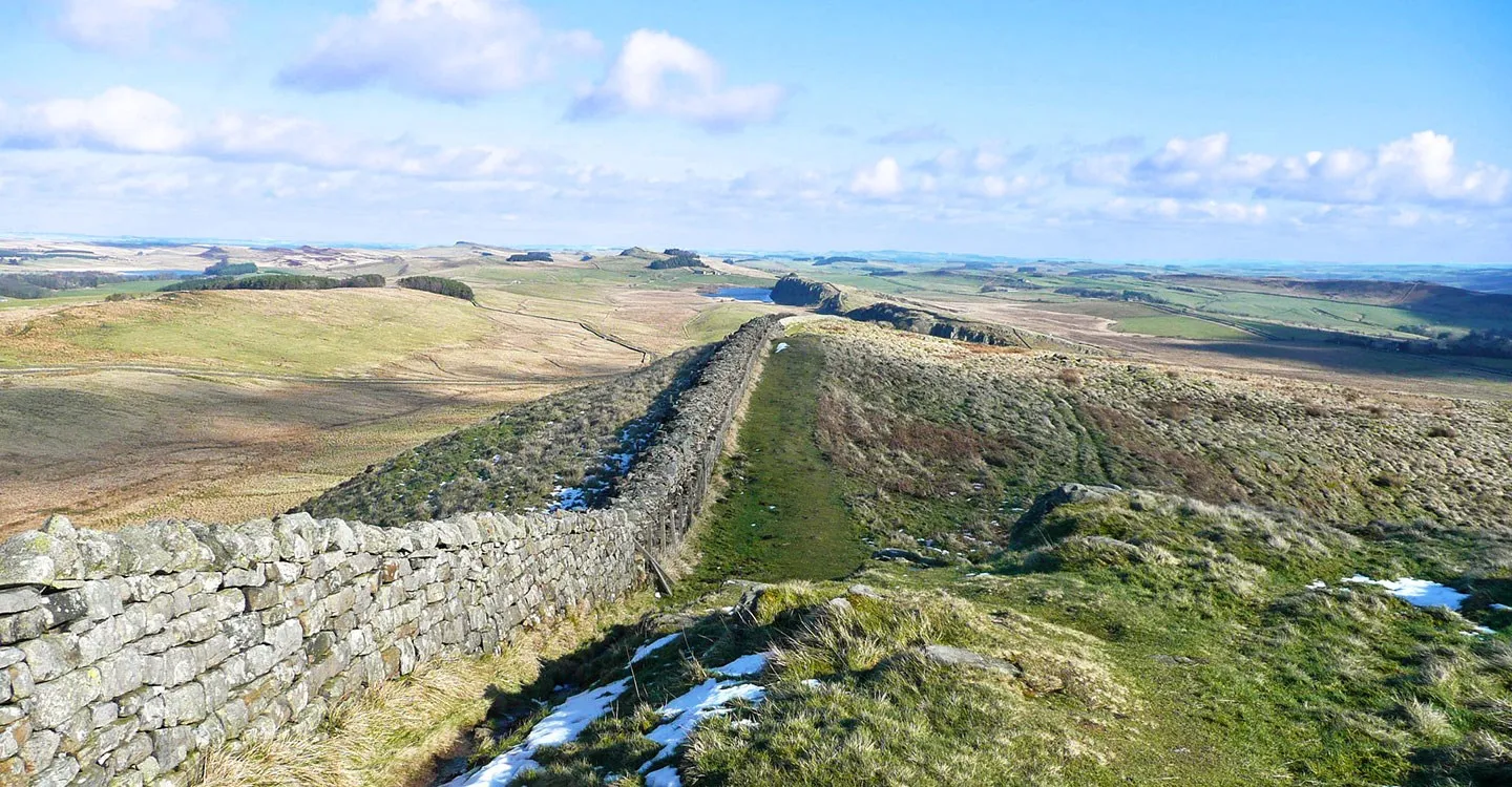 Hadrian's Wall at Winshields running along a grassy ridge with patches of snow, Crag Lough and the moors beyond