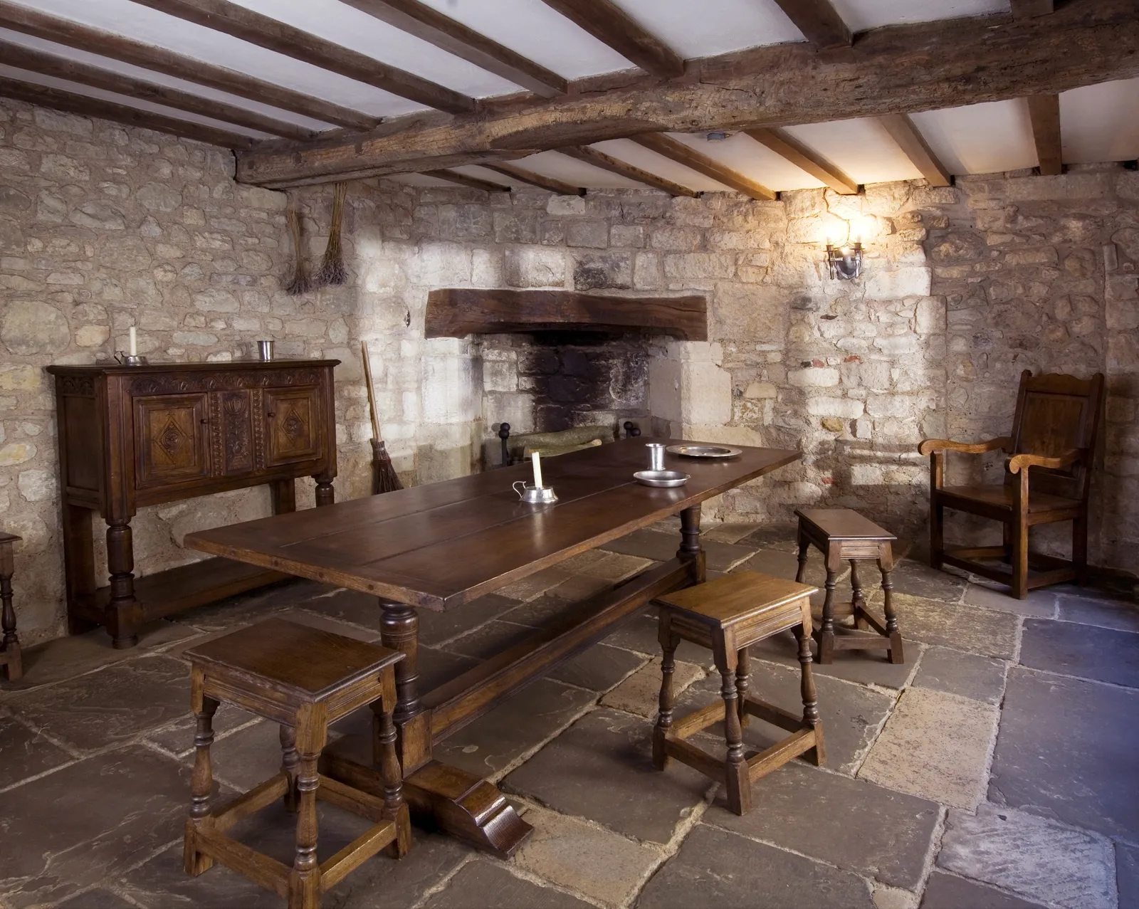 A 16th-century room at Yarmouth Castle with a beamed ceiling, stone walls, a wide fireplace, an oak table, stools and a carved cupboard