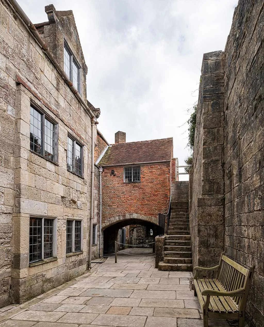 A narrow flagstoned courtyard inside Yarmouth Castle between tall stone walls, with an arched passage under a brick building, stone steps and a bench